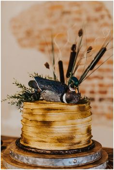 two ducks are sitting on top of a gold wedding cake with feathers and greenery