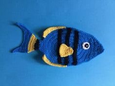 a crocheted blue and yellow fish is on a blue surface with black stripes