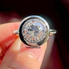 a person holding a ring with a diamond in it's center and surrounded by small round diamonds