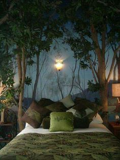 a bed with pillows and green blankets in a room that has trees on the wall