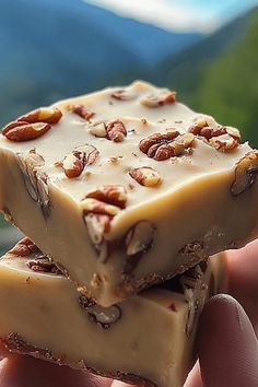 two pieces of white chocolate with pecans on top are held in someone's hand