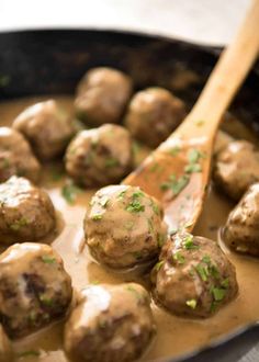 meatballs and gravy are being cooked in a skillet with a wooden spoon