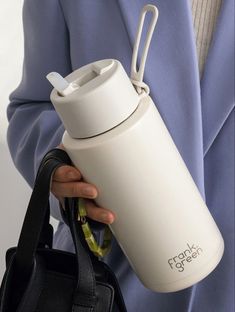 a person in a blue suit holding a white water bottle and black handbag with the words frank green on it