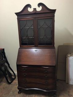 an old wooden desk with glass doors and drawers on the top, next to a cardboard box