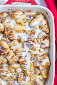 cinnamon rolls with icing in a white casserole dish on a red cloth