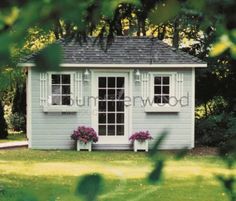 a small white shed sitting in the middle of a lush green field