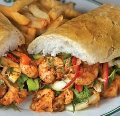 a sandwich with shrimp and veggies is on a plate next to some bread