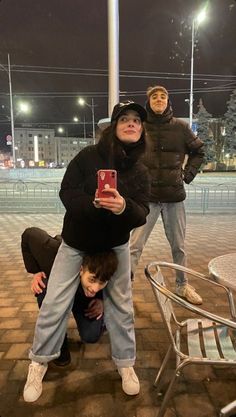 three people posing for a photo in front of a street light at night with one person holding up a cell phone