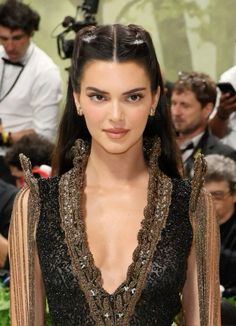 a woman with long dark hair wearing a black and gold dress on the red carpet