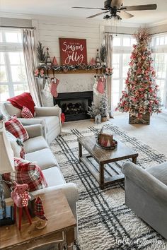 a living room decorated for christmas with red and white decorations on the fireplace, couches, coffee table, and tree