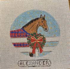 a cross - stitch picture of a horse with a christmas wreath in front of it