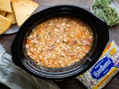 a crock pot filled with beans and ham next to some crackers on a table