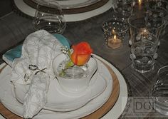 a white plate topped with a vase filled with an orange flower next to other plates and glasses