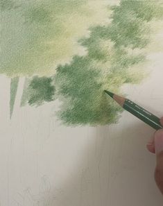 a person holding a pencil in their left hand and drawing on paper with green ink