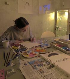 a woman is sitting at a table with some art supplies and watercolors on it