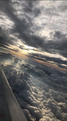 the wing of an airplane as it flies through the sky with clouds and sun peeking out