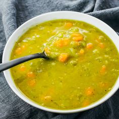 a white bowl filled with soup and carrots on top of a blue cloth next to a spoon