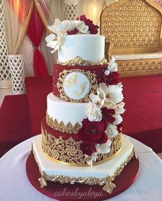 a three tiered wedding cake with red and white flowers on the top, gold trim