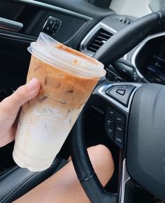 a person is holding a cup in their hand and driving a car with the steering wheel behind them