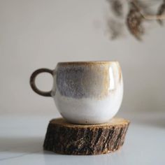 a white and brown cup sitting on top of a piece of wood next to a plant