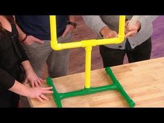 three people standing around a wooden table with yellow and green pipes on top of it