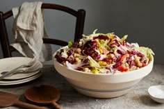 a white bowl filled with salad sitting on top of a table next to two wooden spoons