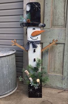 a snowman with a top hat and scarf standing in front of a metal trash can