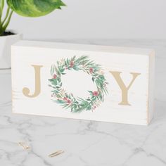 a wooden block with the word joy painted on it and a potted plant next to it