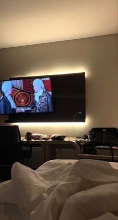 a flat screen tv mounted on the wall above a bed in a room with white sheets