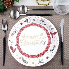 a white plate with merry christmas written on it next to black utensils and silverware