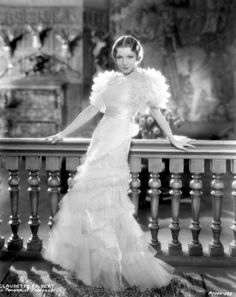 an old photo of a woman in a white dress standing on a balcony with her hands on the railing