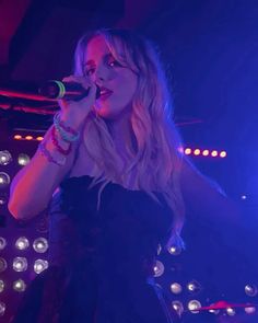 a woman in a black dress holding a microphone up to her mouth while standing on stage