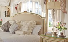 a bed with lots of pillows on top of it next to a dresser and window