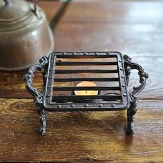 a tea light holder with a candle in it on a wooden table next to a kettle