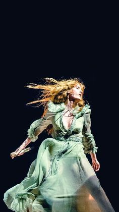 a woman in a long green dress is dancing on the stage with her hair blowing in the wind