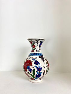 a white vase with blue, red and green flowers painted on the outside of it