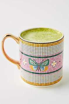 a cup with a butterfly painted on the side and gold trim around the edge, sitting on a white surface