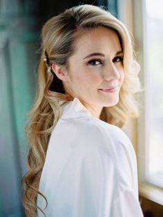 a woman with long blonde hair standing in front of a window wearing a white shirt