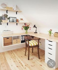 a desk with some flowers on top of it and shelves in the corner behind it