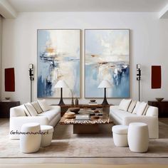 a living room filled with white couches and two large paintings on the wall above them