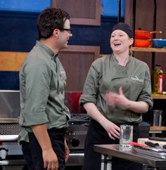 two chefs are talking to each other in front of a stove and counter with utensils on it