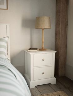 a white nightstand with a lamp on top of it next to a bed in a bedroom