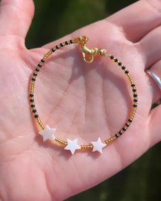 a hand holding a gold and black beaded bracelet with two stars on the side