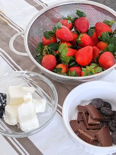 strawberries, chocolate and marshmallows sit in bowls on a tablecloth