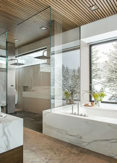 a bathroom with a tub, sink and large window overlooking the snow covered trees outside