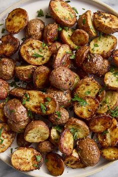 a white plate topped with cooked potatoes covered in herbs and garnished with parsley