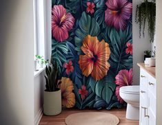 a bathroom with a floral shower curtain and rug in front of the toilet, next to a potted plant