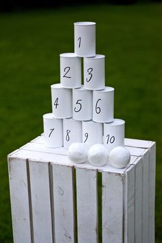 a stack of white cups sitting on top of a wooden crate in the grass with numbers written on them