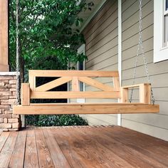 a wooden porch swing sitting on top of a wooden deck next to a tree and house