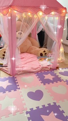 a teddy bear sitting in a pink bed with white curtains and lights on the canopy